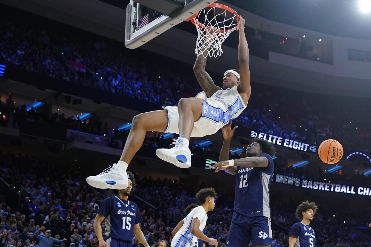 North Carolina's Armando Bacot hangs on the rim after a dunk in front of Saint Peter's Clarence Rupert.