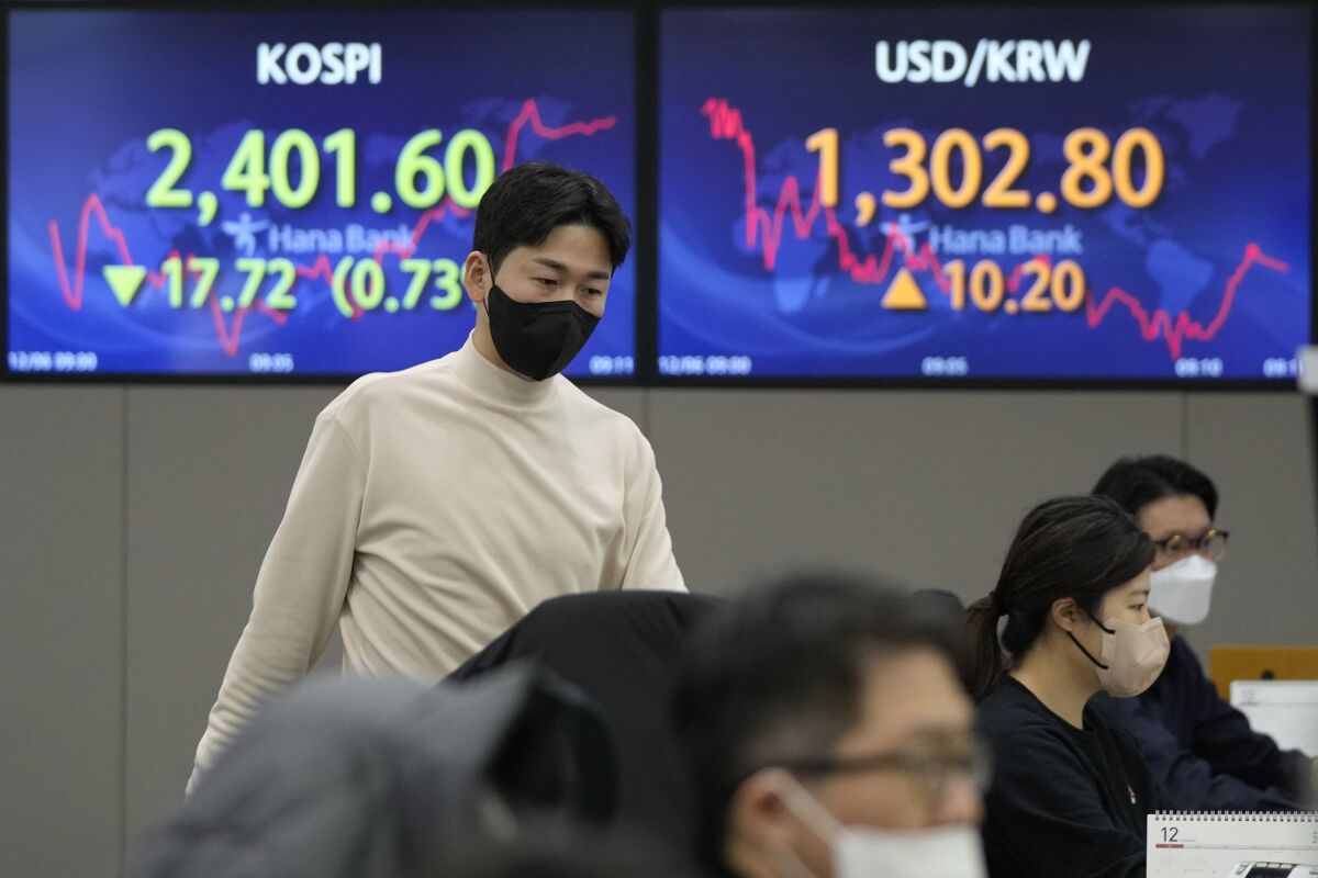 A currency trader passes by screens showing the Korea Composite Stock Price Index (KOSPI), left, and the exchange rate of South Korean won against the U.S. dollar at the foreign exchange dealing room of the KEB Hana Bank headquarters in Seoul, South Korea, Tuesday, Dec. 6, 2022. Stocks were mostly lower in Asia on Tuesday after Wall Street pulled back as surprisingly strong economic reports highlighted the difficulty of the Federal Reserve’s fight against inflation. (AP Photo/Ahn Young-joon)
