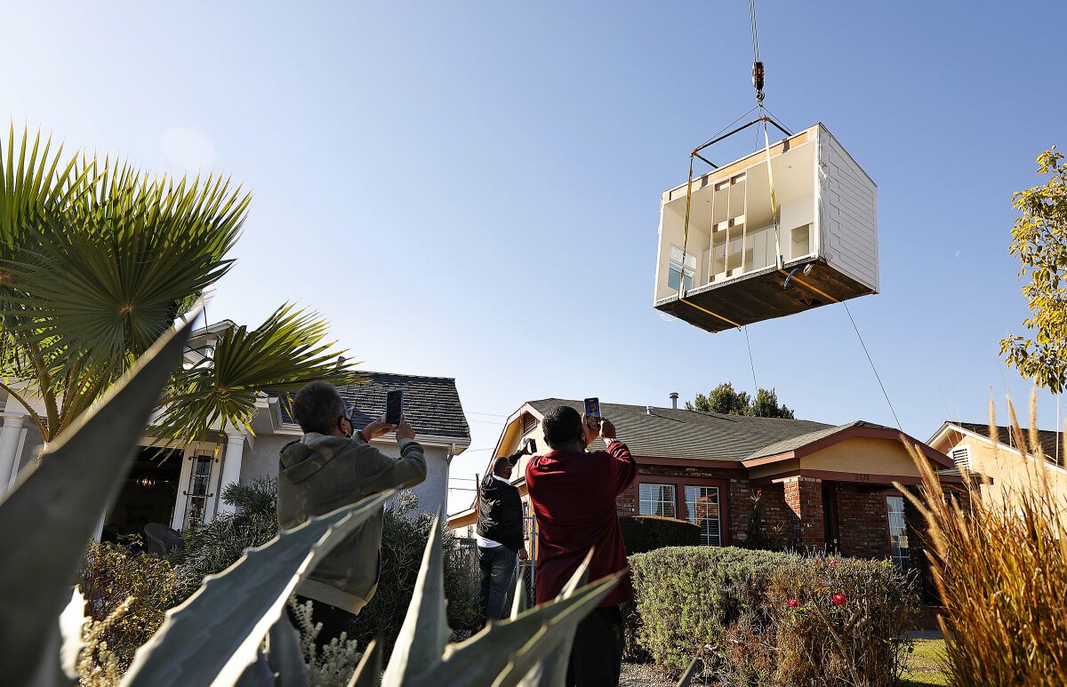 An ADU on a crane is lifted over homes into a backyard in South L.A.