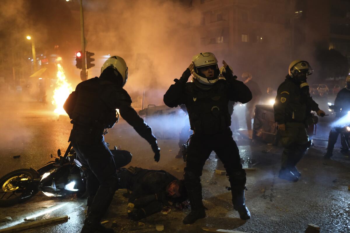 A policeman lays injured on the road as his colleagues react during clashes in Athens, Tuesday, March 9, 2021. Severe clashes broke out Tuesday in Athens after youths protesting an incident of police violence attacked a police station with petrol bombs, and severely injured one officer. (AP Photo/Aggelos Barai)