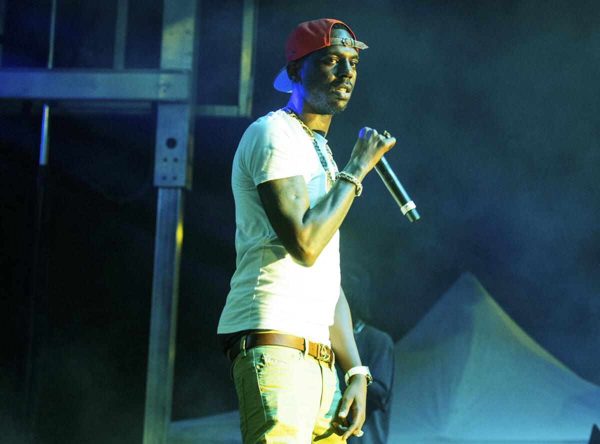 Young Dolph standing on stage wearing a red hat and holding a microphone.