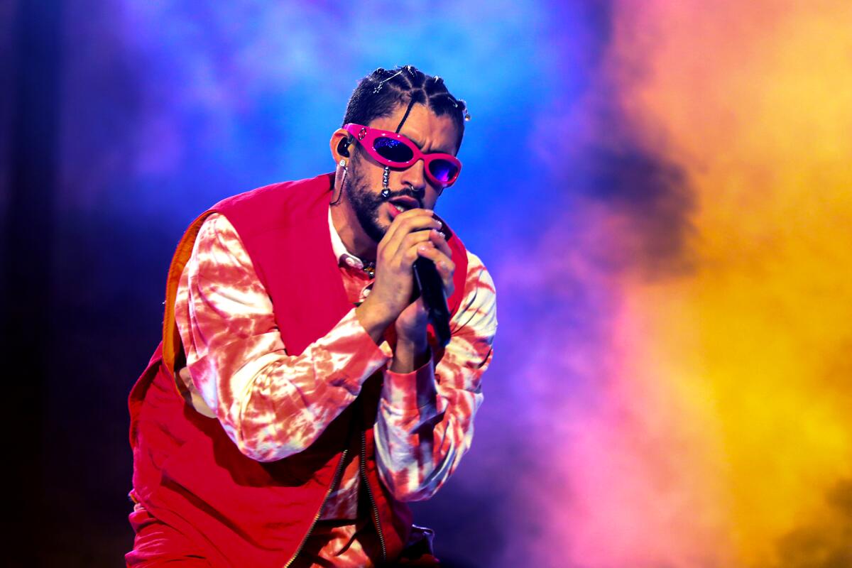 A performer wearing a red and white outfit with red sunglasses sings into a microphone