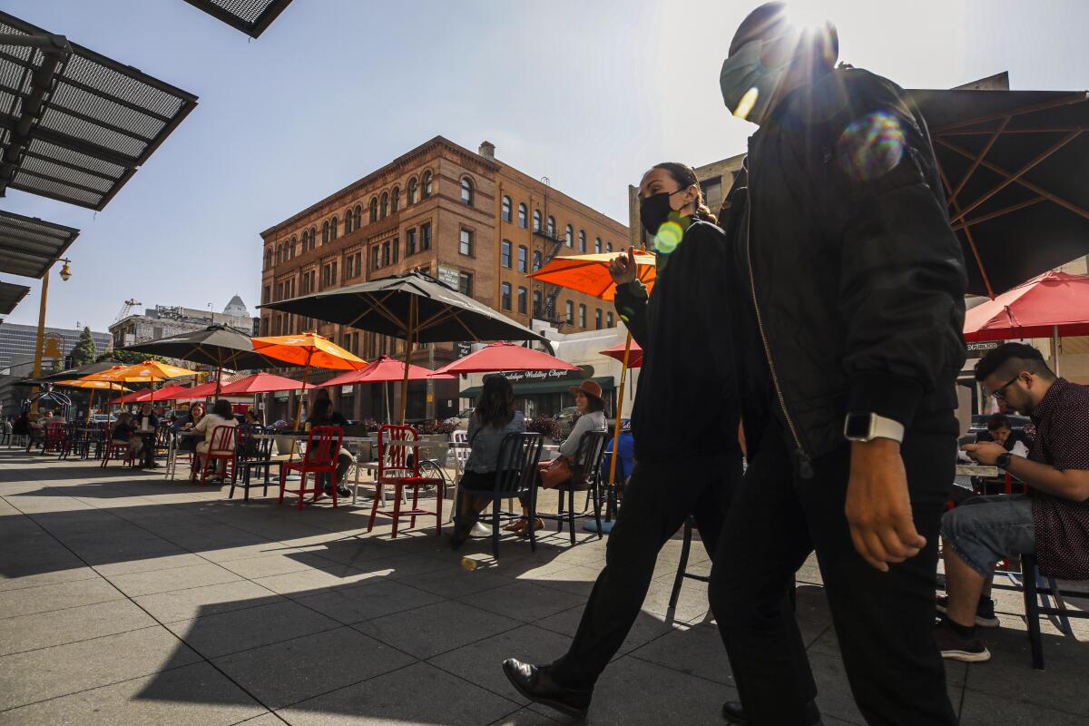 Two people wearing masks walk past diners eating at umbrella-covered tables at Grand Central Market in downtown L.A.