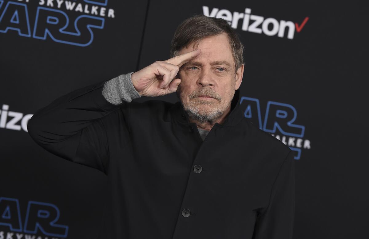 A man in dark clothing salutes onlookers at a movie premiere.