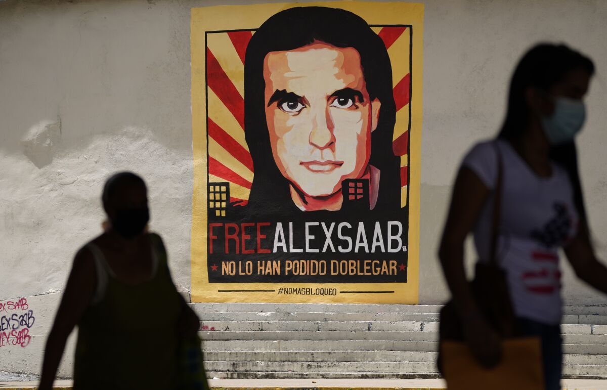 FILE - In this Sept 9, 2021 file photo, pedestrians walk near a poster asking for the freedom of Colombian businessman and Venezuelan special envoy Alex Saab, in Caracas, Venezuela. The Venezuelan government added Saab on Tuesday, September 14, 2021, to the negotiation team that is meeting with the opposition in Mexico. Saab has was detained in Cabo Verde a year ago and is facing extradition to the US for money laundering. (AP Photo/Ariana Cubillos, File)