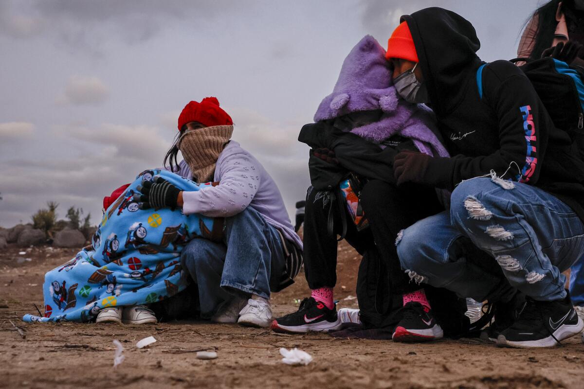 Two people huddle on the ground clutching children in thick winter gear 