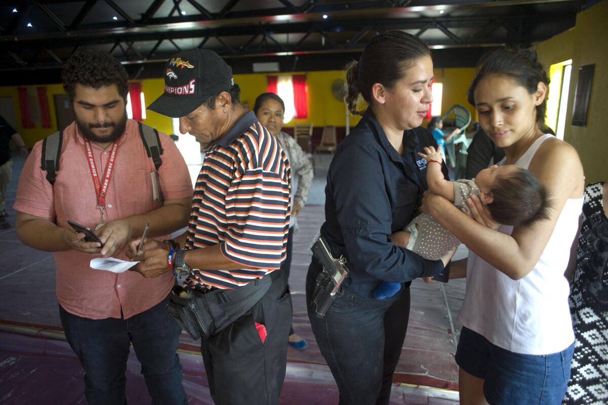 Tamara Arias, second from right, an agent with the human trafficking division of the Baja California State Attorney General's Office, hands back Alexander, the 2-month-old son of Milagro de Jesus Enriquez, right, after a presentation by various state and federal officials at the Agape Misin Mundial shelter for migrants.