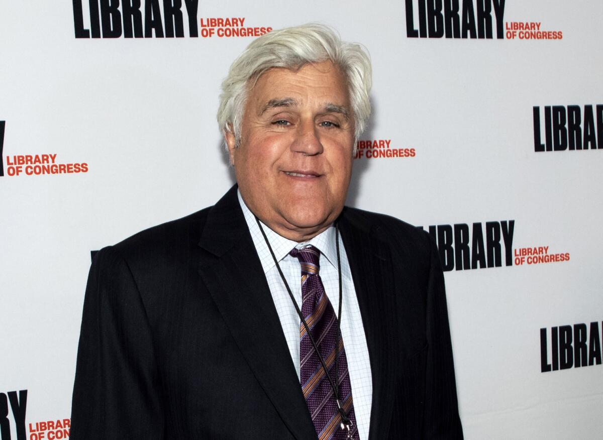 A white-haired man wearing a coat and tie smiles while standing in front of a Library of Congress backdrop