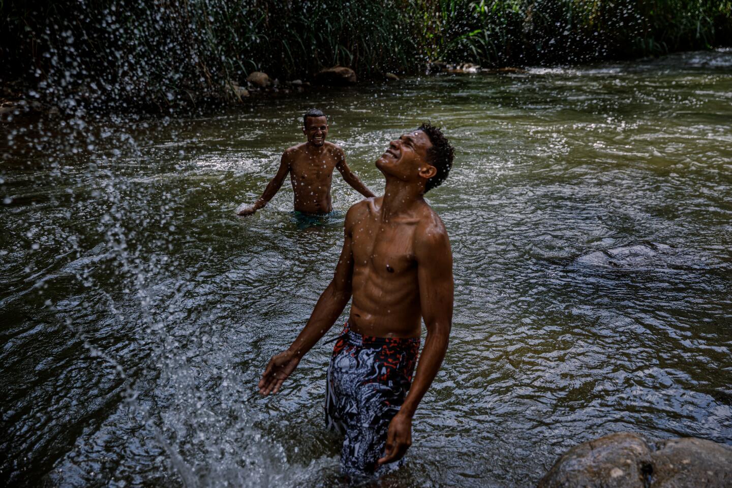 Joel Samora, 40, left, and Elieser Galarraga, 28, splash in a river near a campground shelter for Venezuelan migrants in Bochalema, Colombia.
