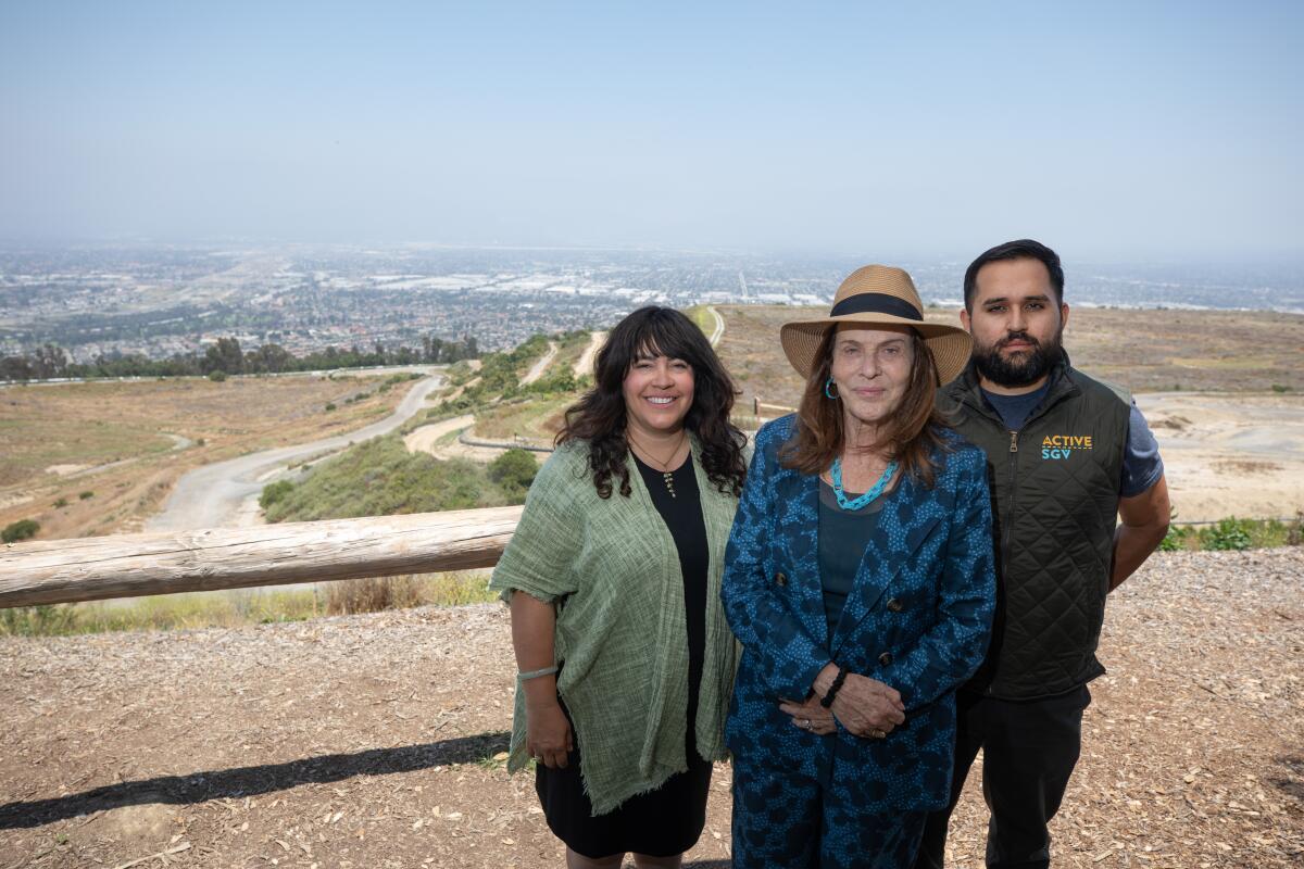 Three people — two women and one man — stand at the top of a scrubby hill that overlooks the San Gabriel Valley