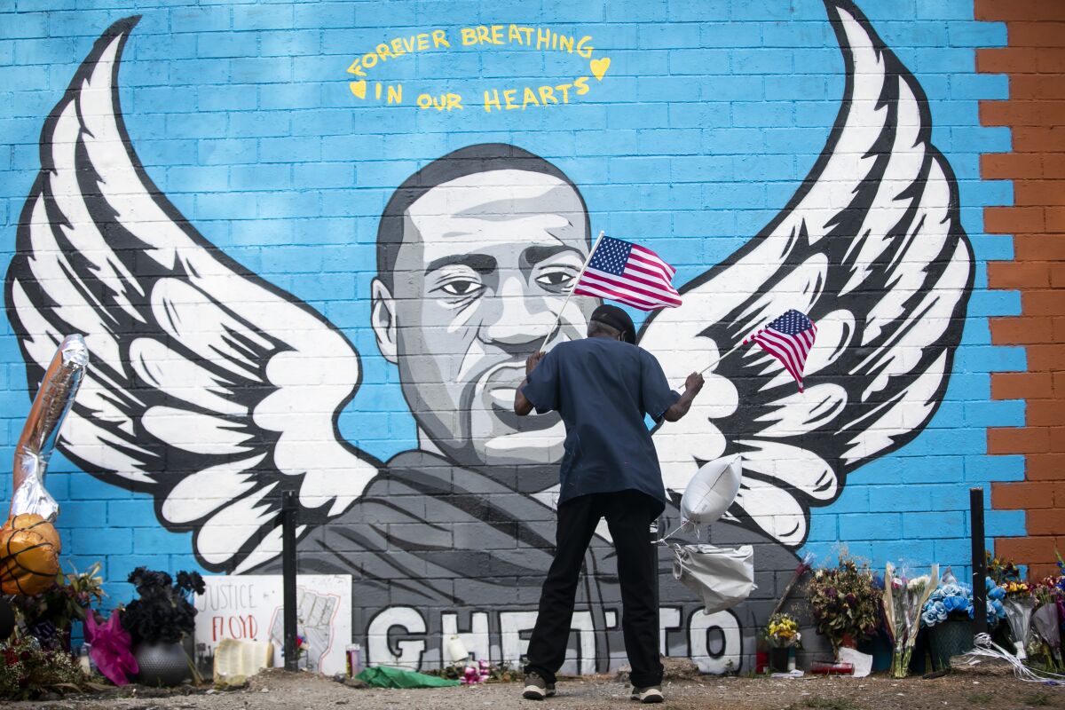 A man places two flags at the foot of the mural honoring George Floyd in Houston.