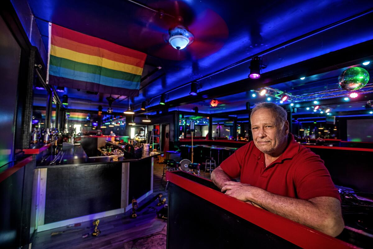 Steve Terradot inside his bar, the Boulevard, bathed in blue lights with a Pride flag on the wall.