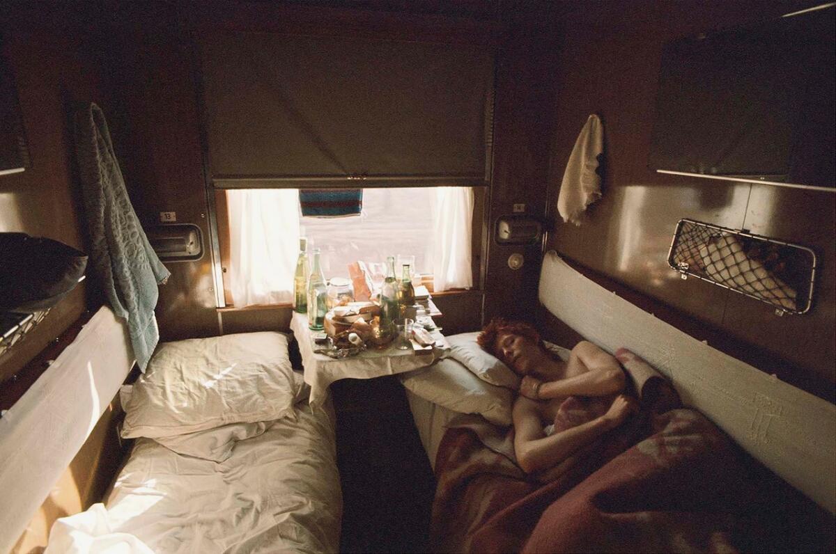 An overhead shot shows David Bowie sleeping in a narrow train cabin next to a tray of food and drinks.