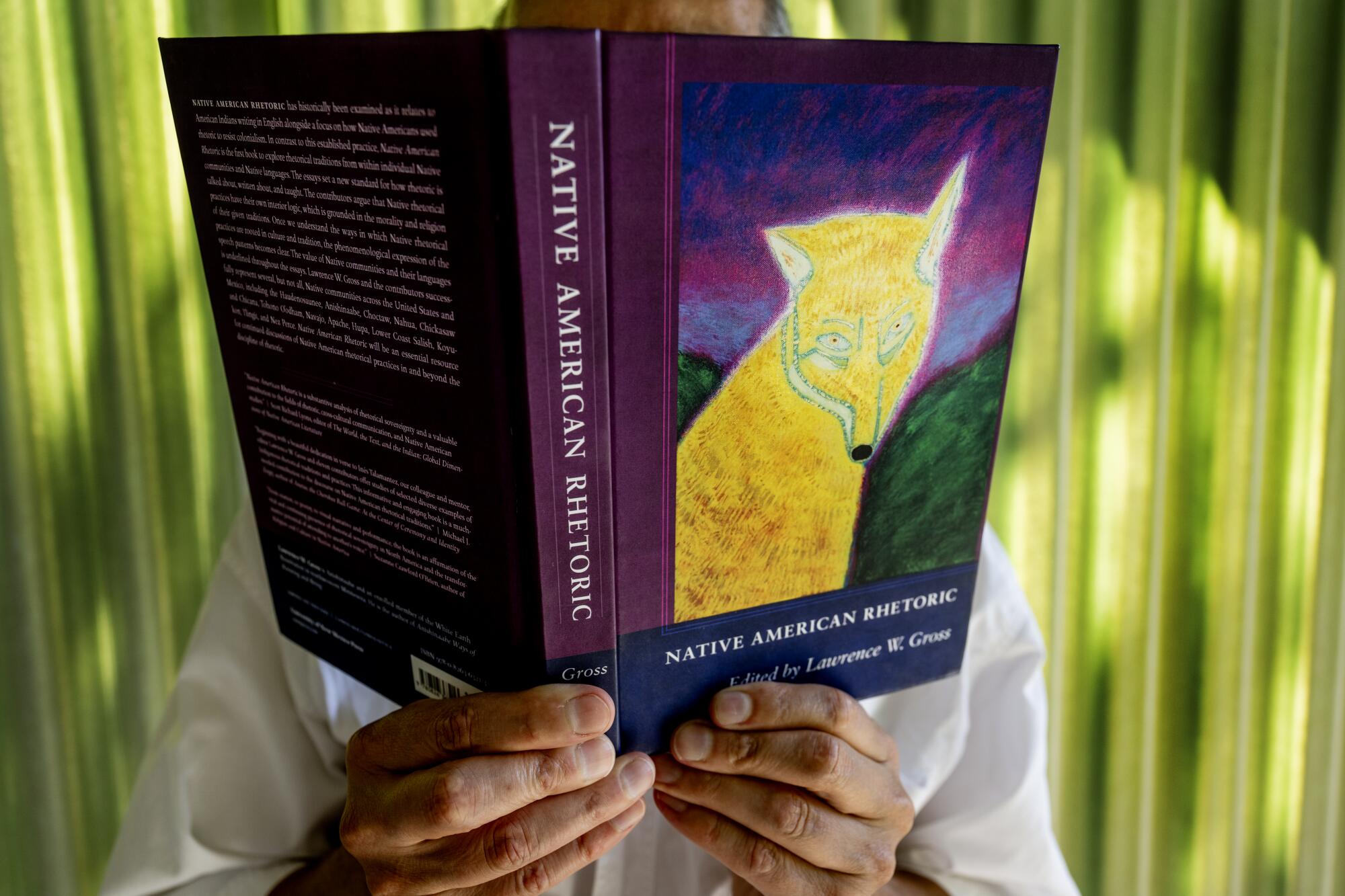 A man holds an open book with a drawing of a yellow-colored fox on its cover, his face behind the book
