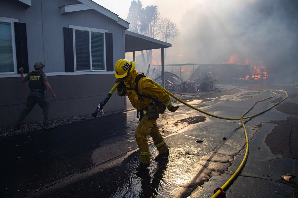 A firefighter hauls a hose in the Villa Calimesa Mobile Home Park, where the Sandalwood fire destroyed 74 homes and buildings.
