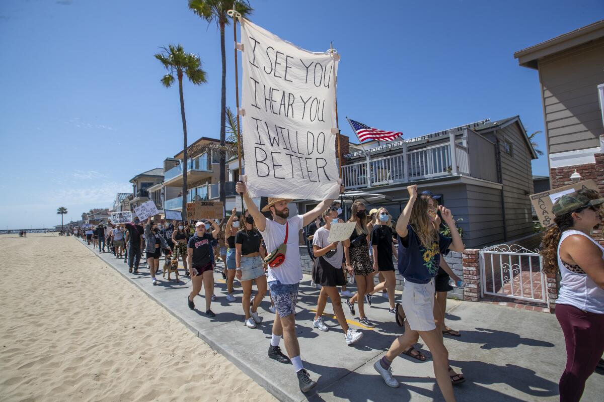 Protesters march down a beachfront bike path in Newport Beach. A sign reads "I see you. I hear you. I will do better."