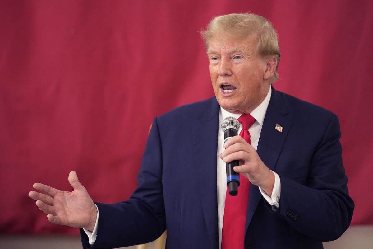 Ex-President Trump speaking as he stands against a red background, holding a microphone and gesturing with his other hand