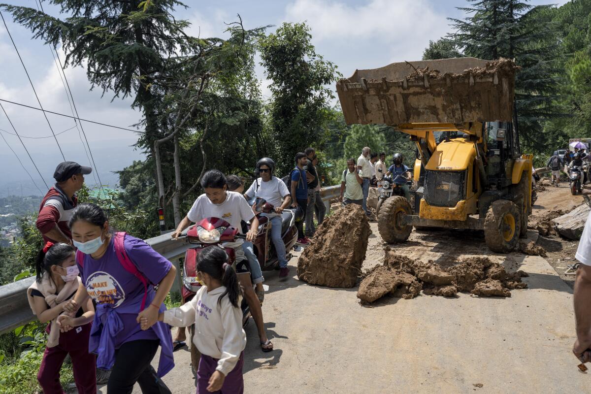 People rush past an earthmover clearing a road of a big rock.