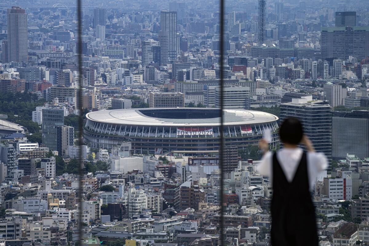 A huge oval stadium with a Tokyo 2020 banner is seen in the distance from a skyscraper observation deck