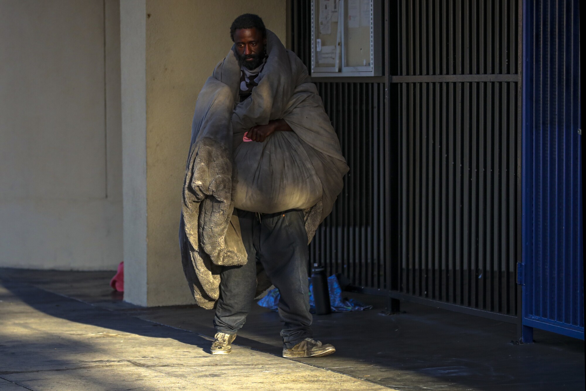 A man walks down the sidewalk wrapped in a heavy blanket.