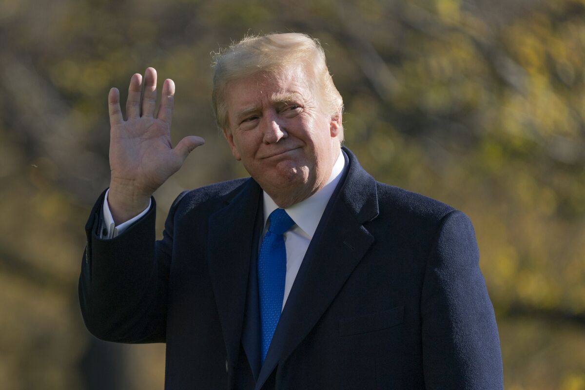 President Trump waves while outdoors with trees behind him. 