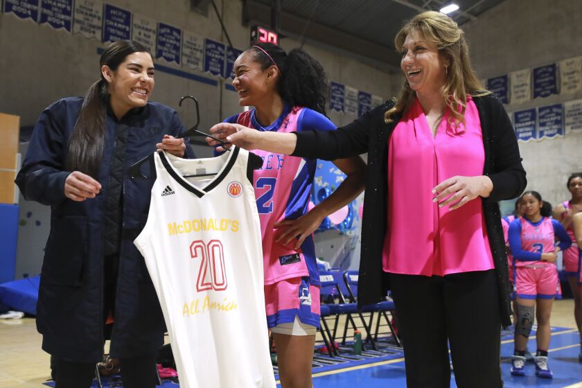 La Jolla Country Day girls basketball coach Terri Bamford, right, hands a Jolla Country Day alumni Kelsey Plum a McDonald's All-American jersey so that Plum can present to La Jolla Country Day basketball player Te-hina Paopao, center, during a short ceremony before the start of La Jolla Country Day's game against Bishop's at La Jolla Country Day School on Friday, February 7, 2020 in San Diego, California.