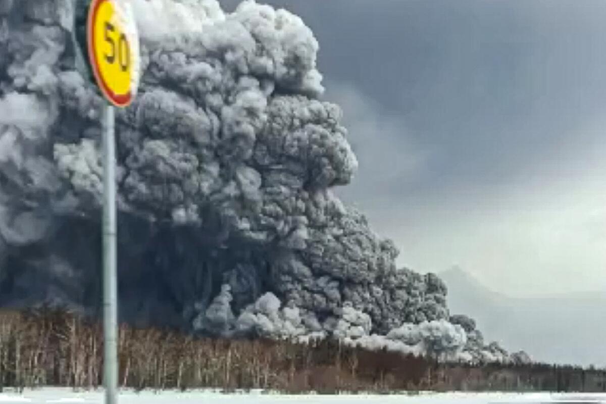 A massive plum of smoke and ash from a volcanic eruption are seen from a roadway. 