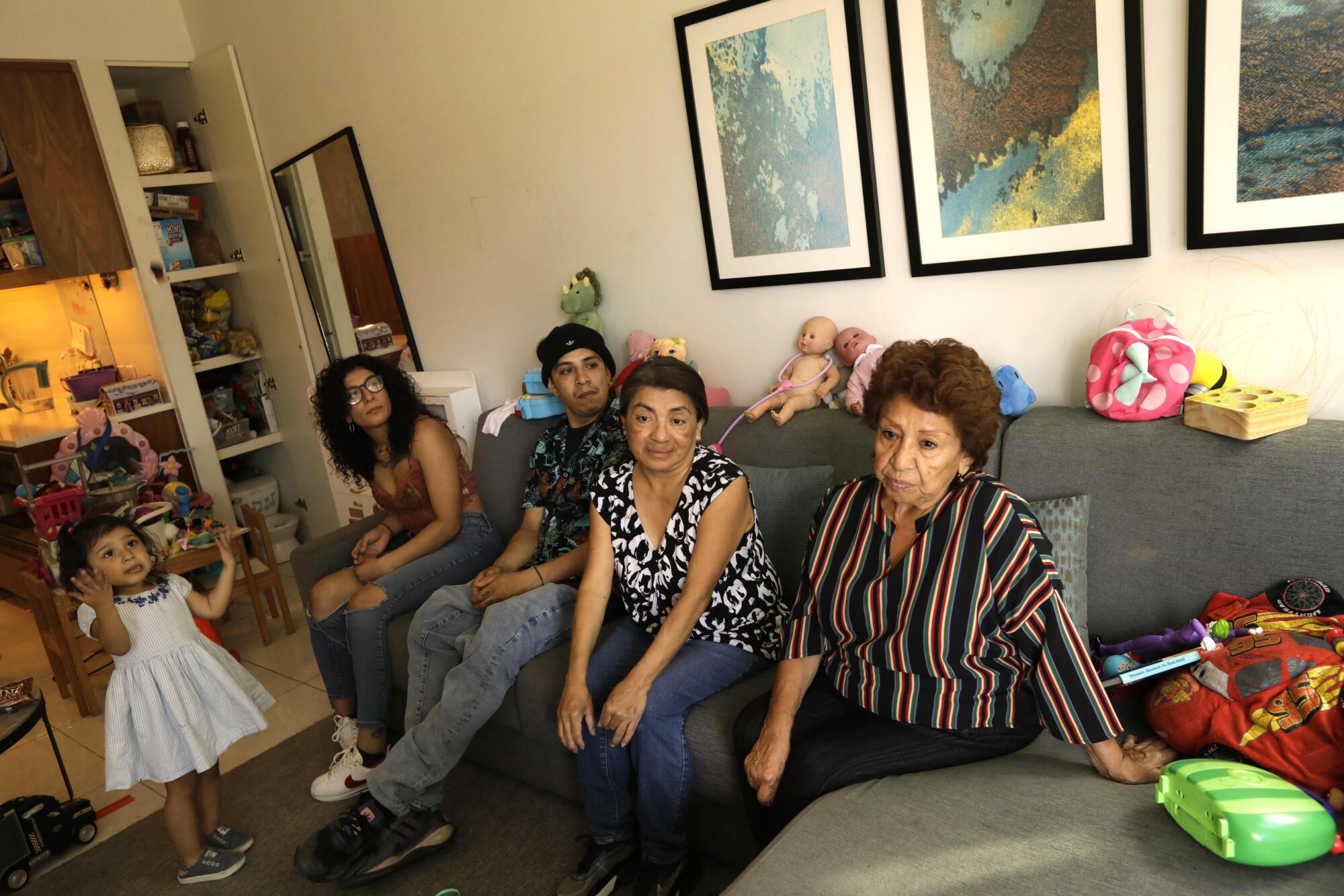 Family members sit on a couch with toys, next to a young girl