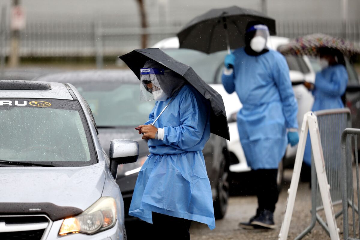 Health workers stand under umbrellas next to cars at a coronavirus testing site.