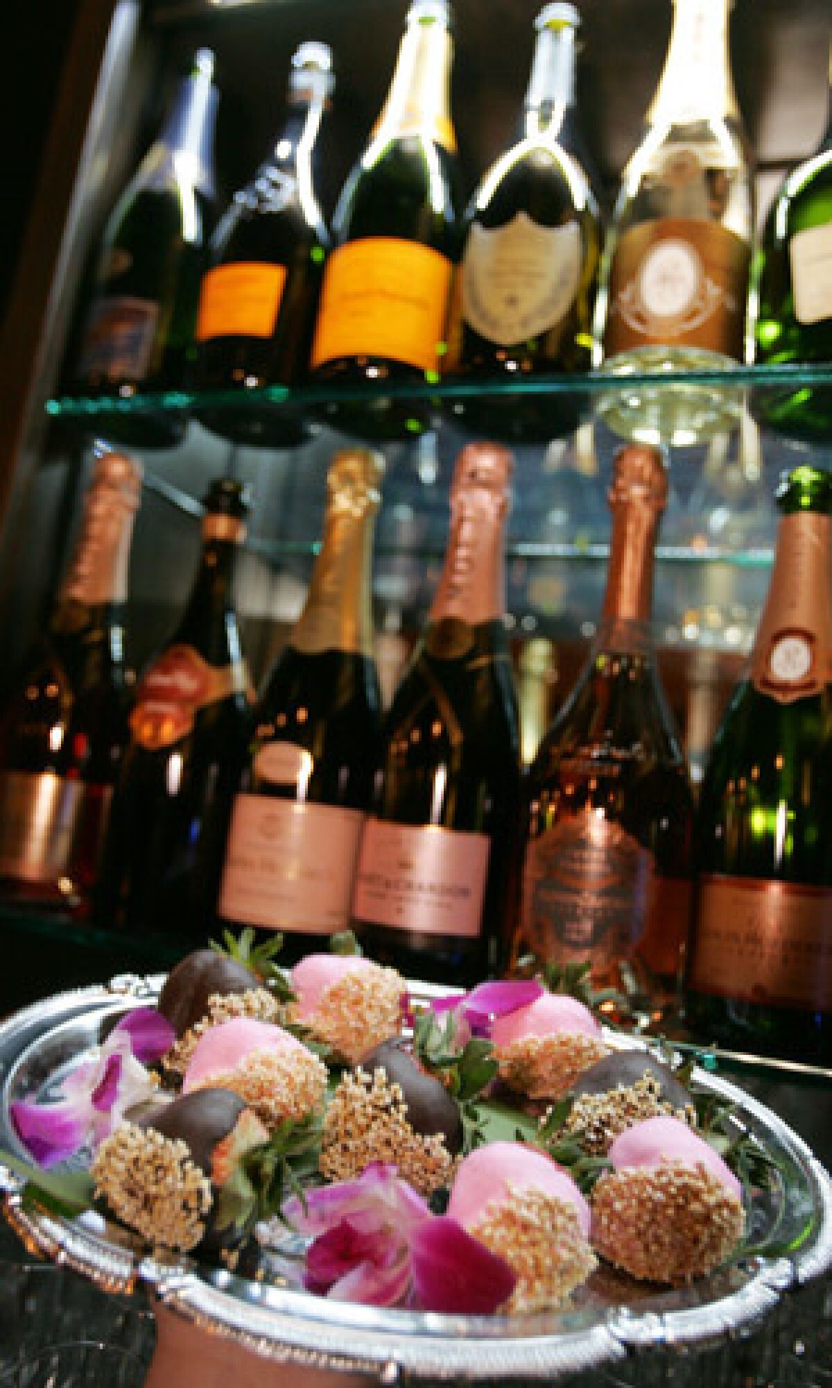 A tray of chocolate-dipped strawberries in front of an array of champagne at POP Champagne & Dessert Bar in Pasadena.