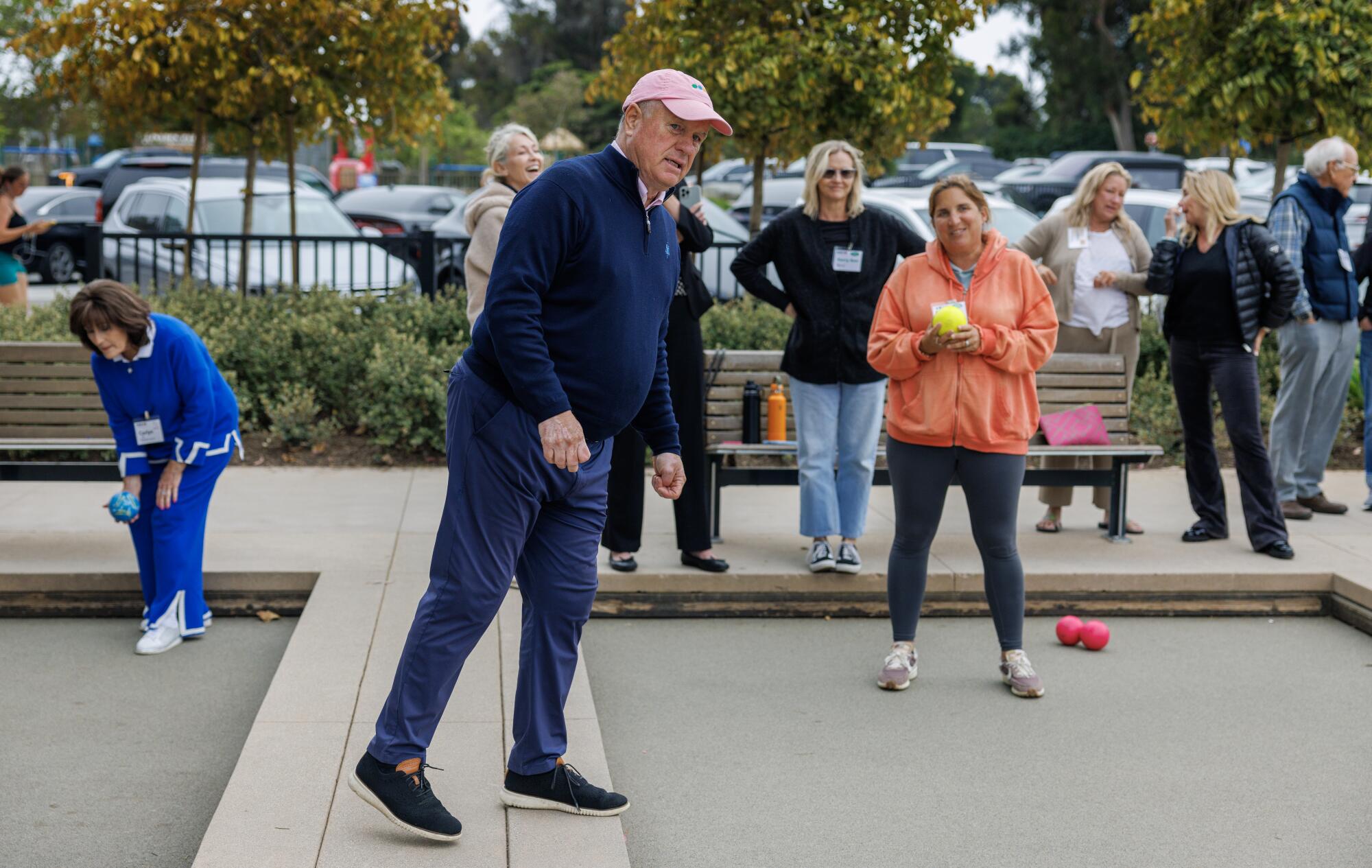 A man watching a game of bocce, surrounded by other bocce players.