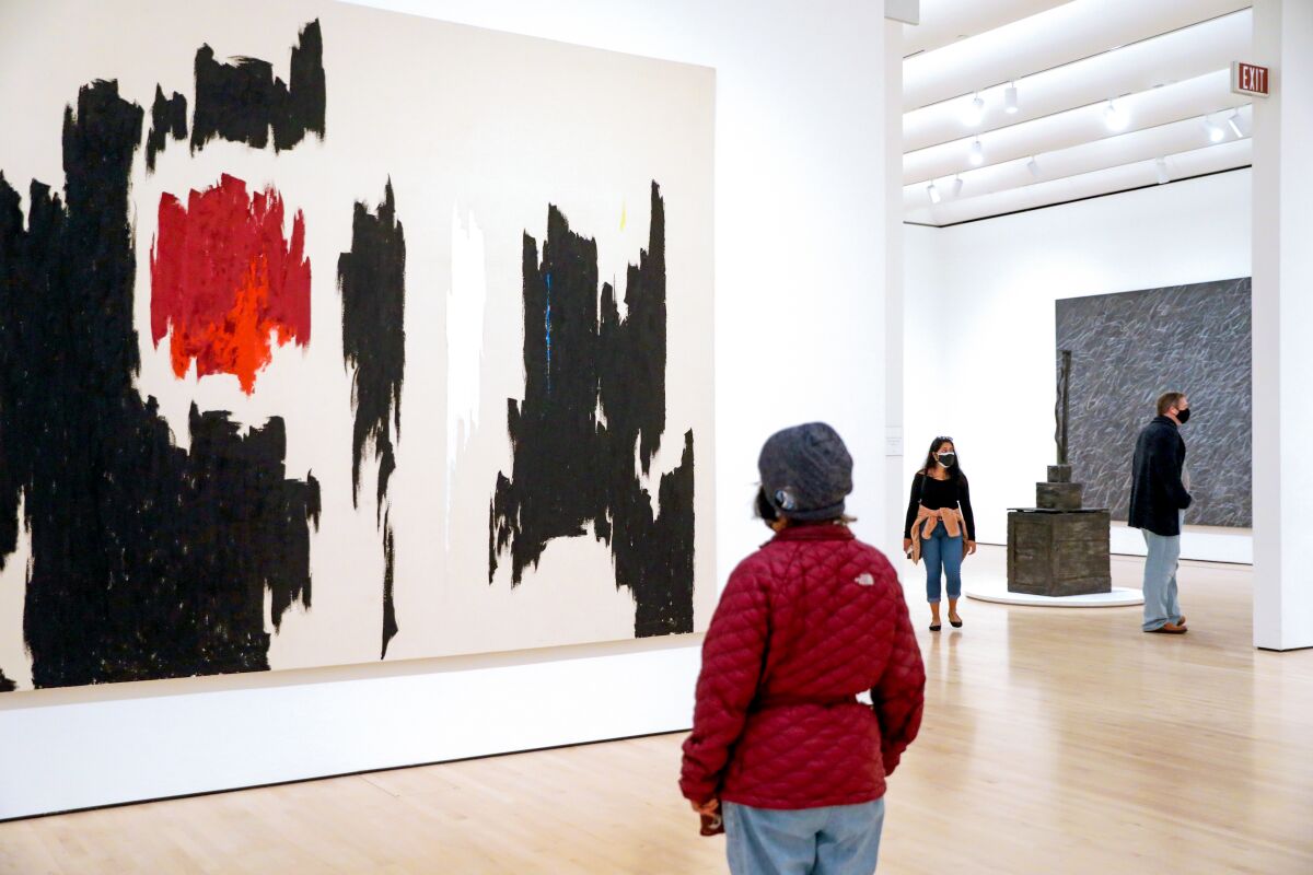 Museum-goers look at modern paintings in a large gallery
