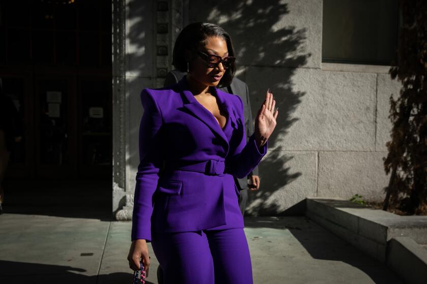 Megan Thee Stallion, real name Megan Pete, walks out of an L.A. courthouse with one palm facing off-camera onlookers