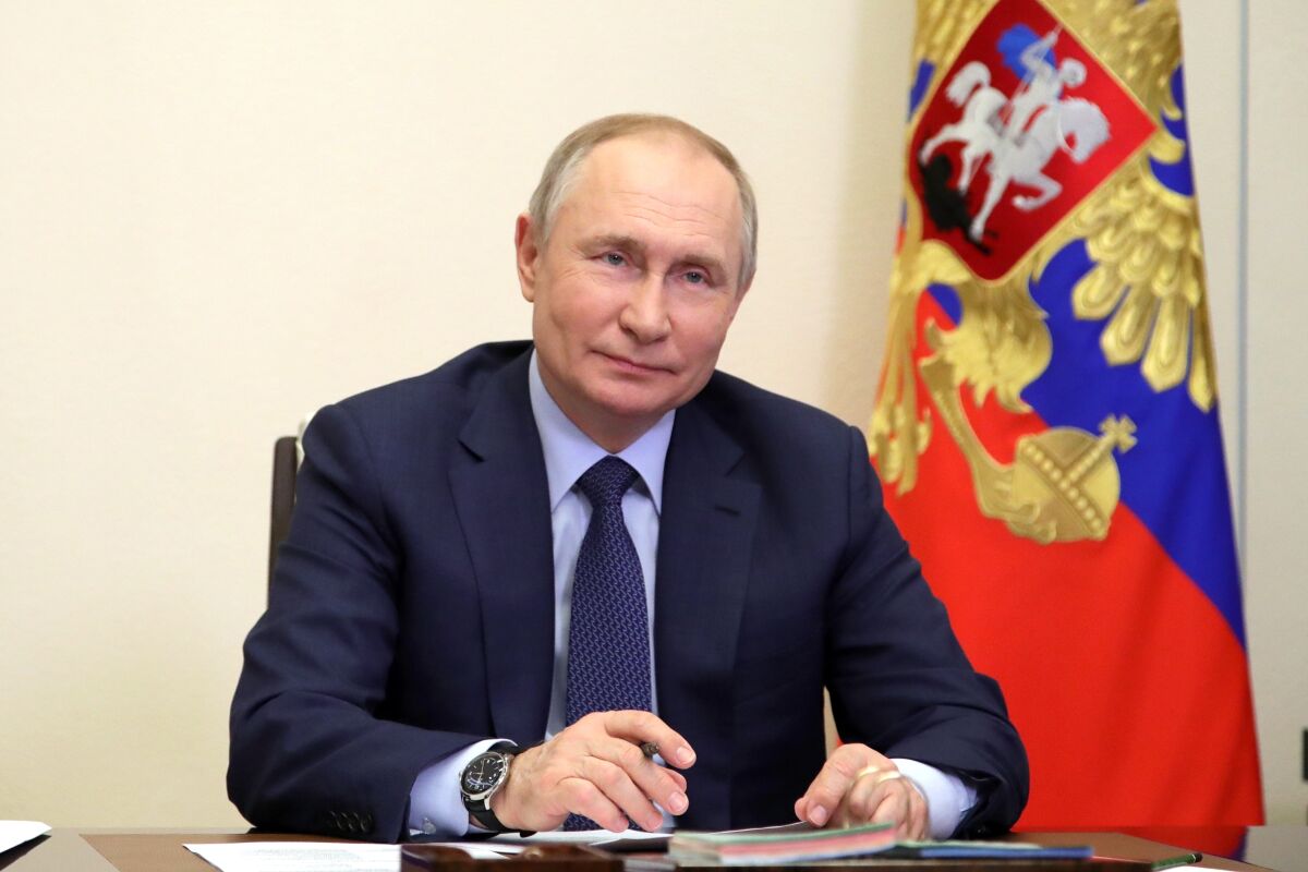 Russian President Vladimir Putin sits at a table with a flag behind him.