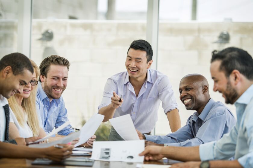 A man smiling and pointing at coworkers in a work meeting
