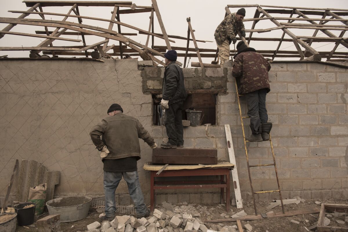 People stand in front of a wall with debris on the ground.