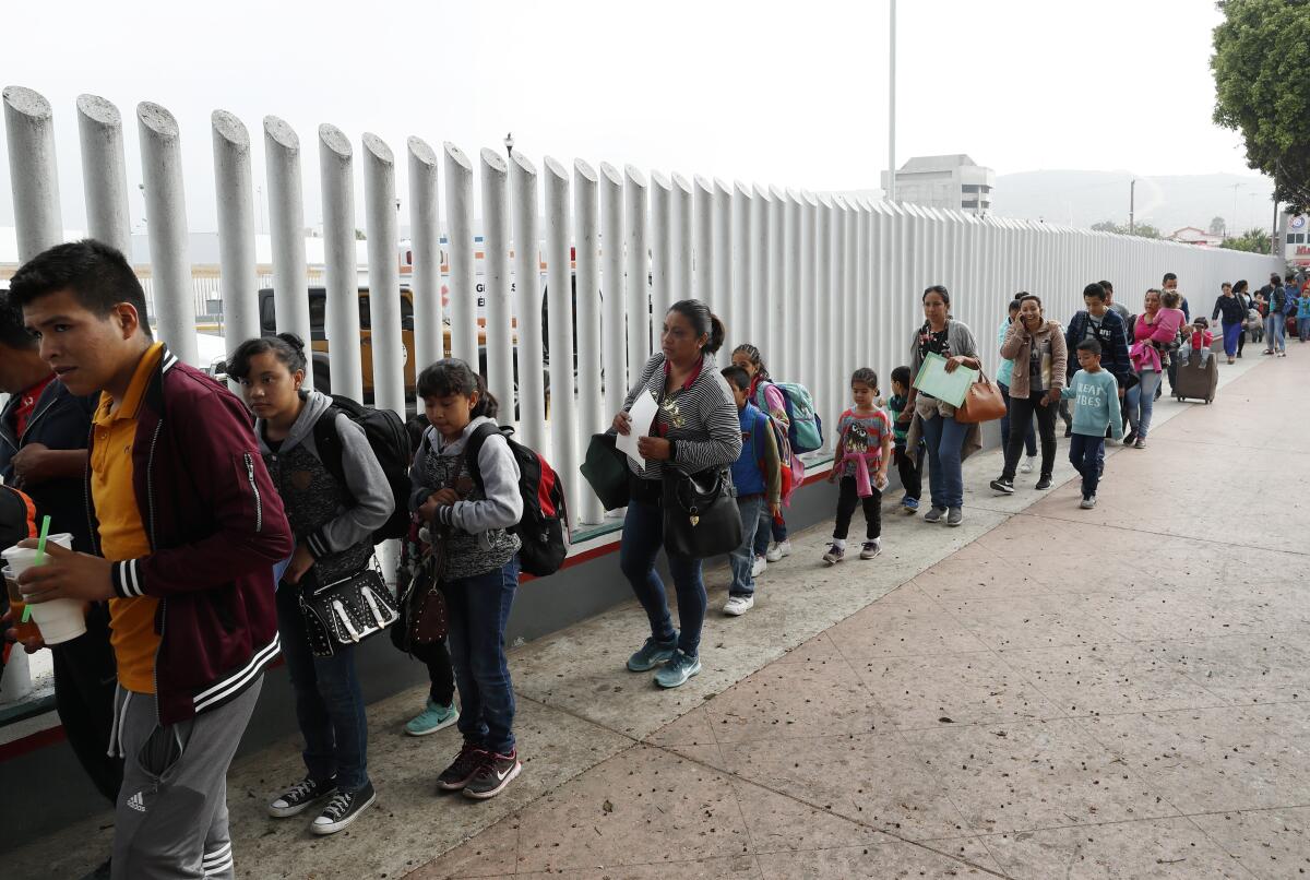 Men, women and children line up at a border fence.