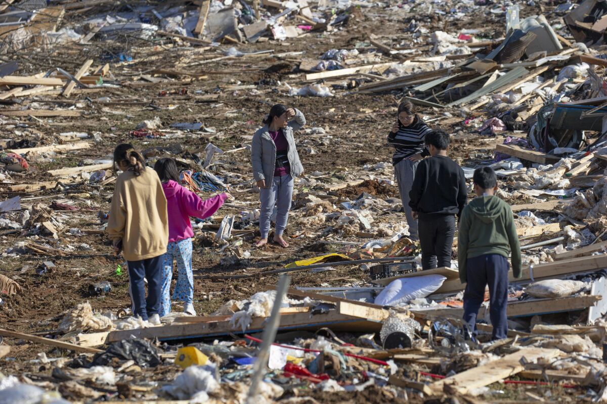 Vung Nuam, center, looks through the remains of her home Tuesday, Dec. 14, 2021, in Bowling Green, Ky. (AP Photo/James Kenney)