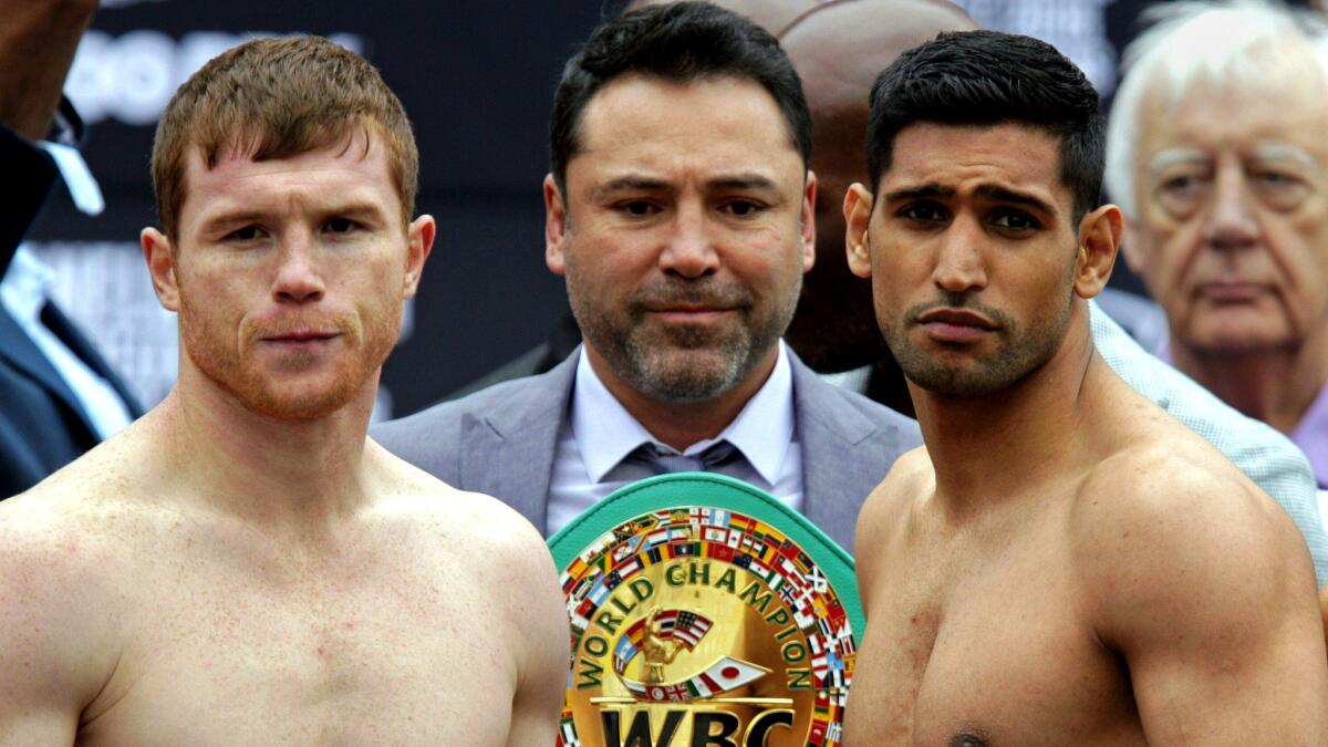 Saul 'Canelo' Alvarez, left, and Amir Khan pose following their weigh-in with promoter Oscar De La Hoya holding the WBC middleweight belt behind them.