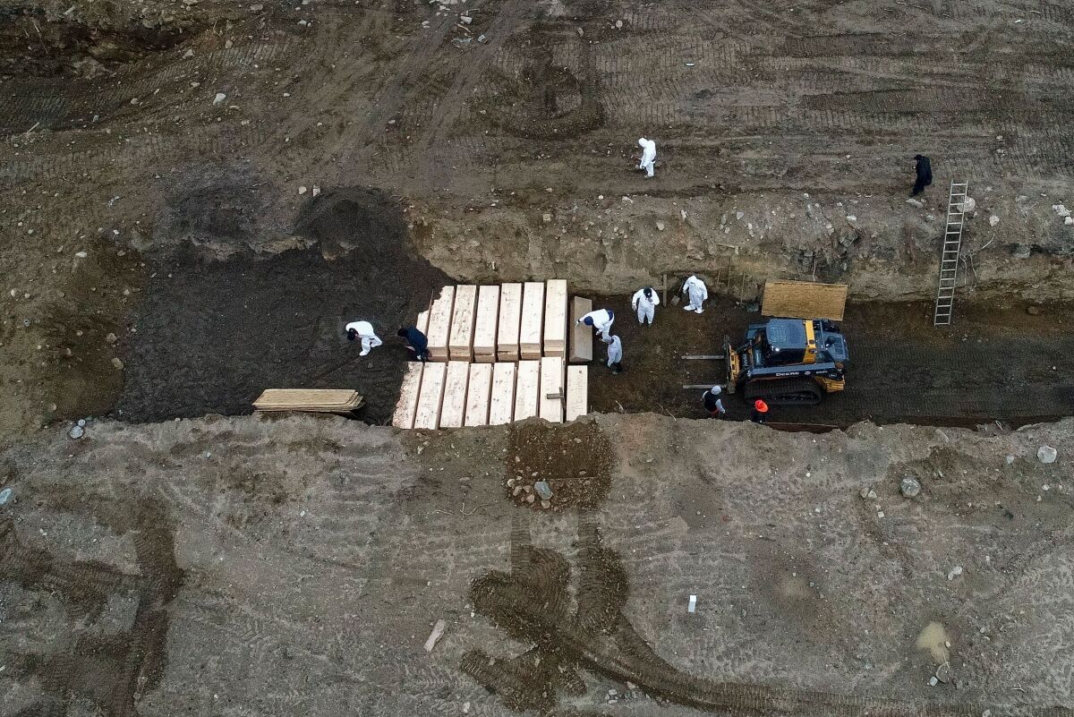 Workers wearing personal protective equipment bury bodies in a trench on Hart Island in New York City last month.