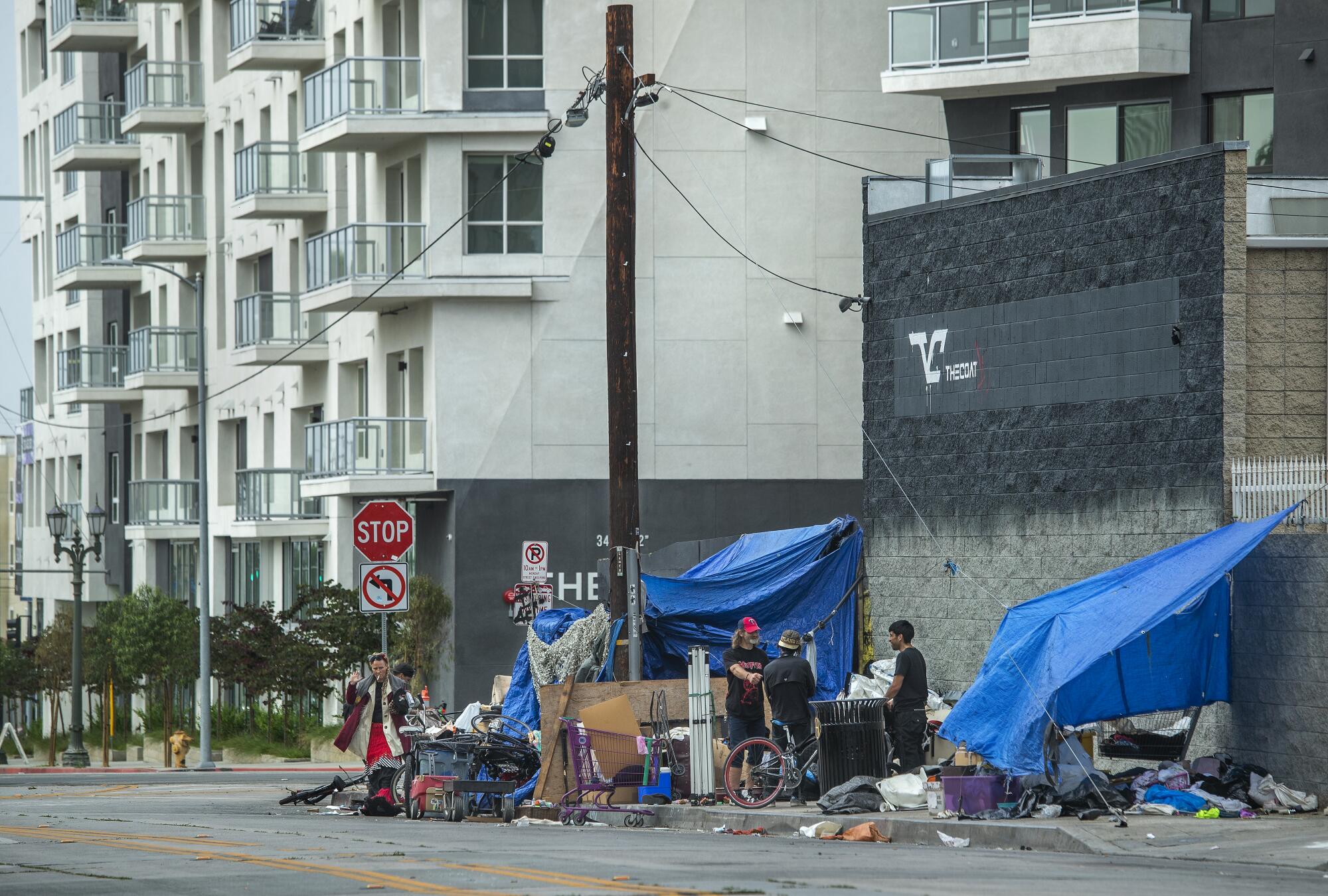 People and tents on the street with a high-rise behind them.