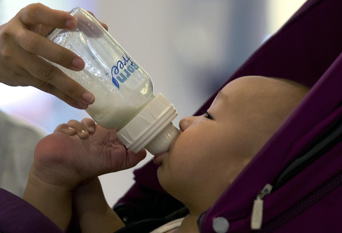 A baby is fed milk from a bottle while sitting in a stroller at a shopping mall in Beijing.