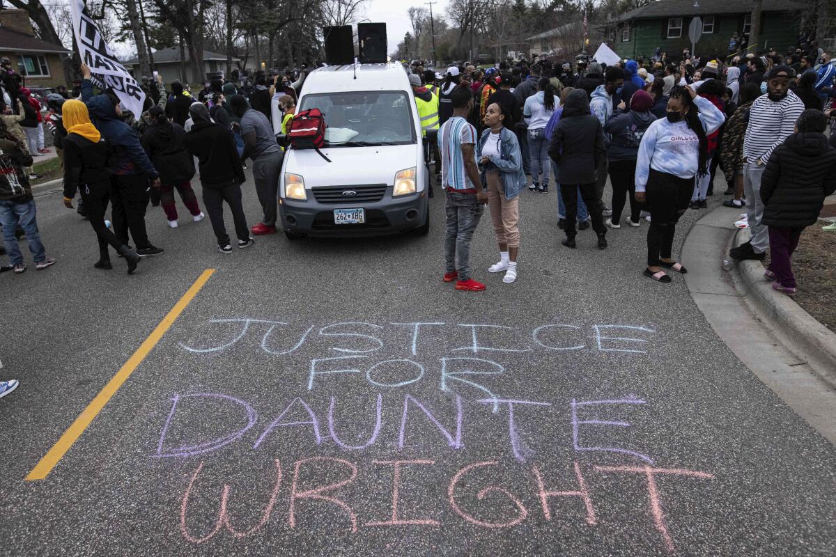 A crowd stands on a roadway where the phrase "Justice for Daunte Wright" is written in chalk.