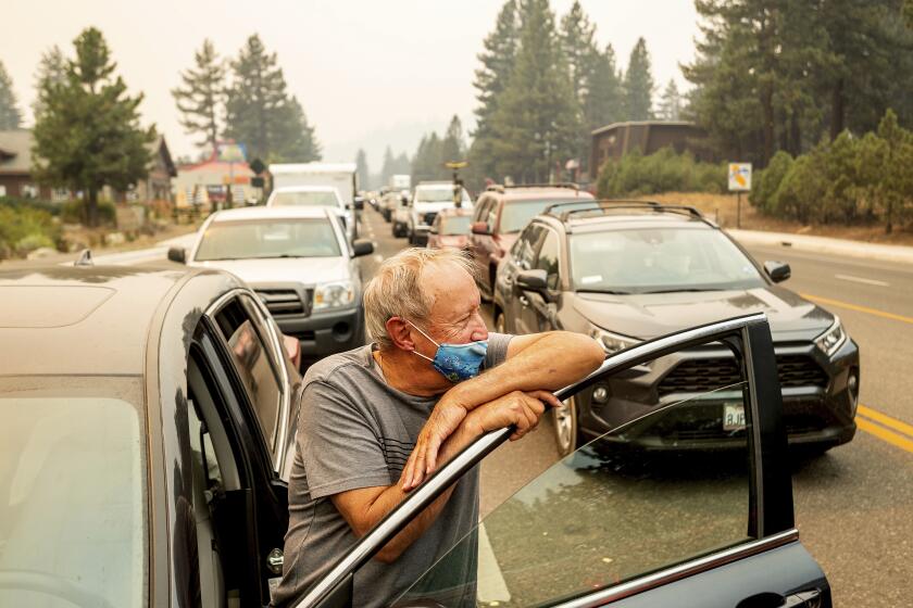 With the Caldor Fire approaching, Jim Mrazek stands outside his vehicle on Highway 50 as evacuee traffic stands still in South Lake Tahoe, Calif., on Monday, Aug. 30, 2021. Mrazek, who was stopped in that spot for more than an hour, said he was considering taking his boat into the lake instead of trying to drive out. (AP Photo/Noah Berger)