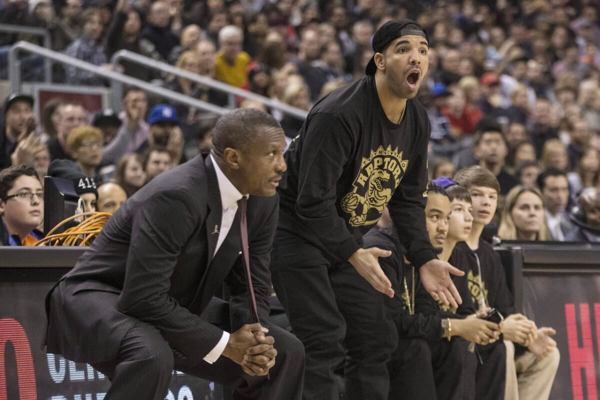 Rapper Drake, center, reacts to a call as he stands with Toronto Raptors Coach Dwane Casey, left, as the Raptors face the Brooklyn Nets in an NBA basketball game Saturday in Toronto.