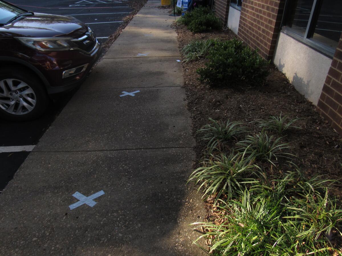 Taped Xs mark the spots on an empty sidewalk where voters are meant to stand. 