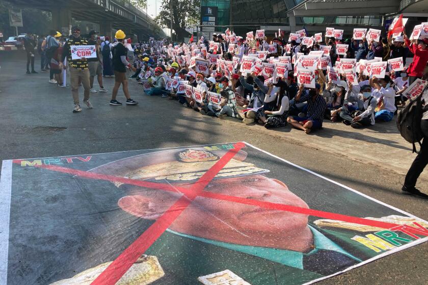 A large image that has an X mark on the face of Commander in chief Senior General Min Aung Hlaing, also Chairman of the State Administrative Council, lies on the road as anti-coup protesters gather outside the Hledan Centre in Yangon, Myanmar, Sunday, Feb. 14, 2021. Daily mass street demonstrations in Myanmar are on their second week, with neither protesters nor the military government they seek to unseat showing any signs of backing down from confrontations. (AP Photo)