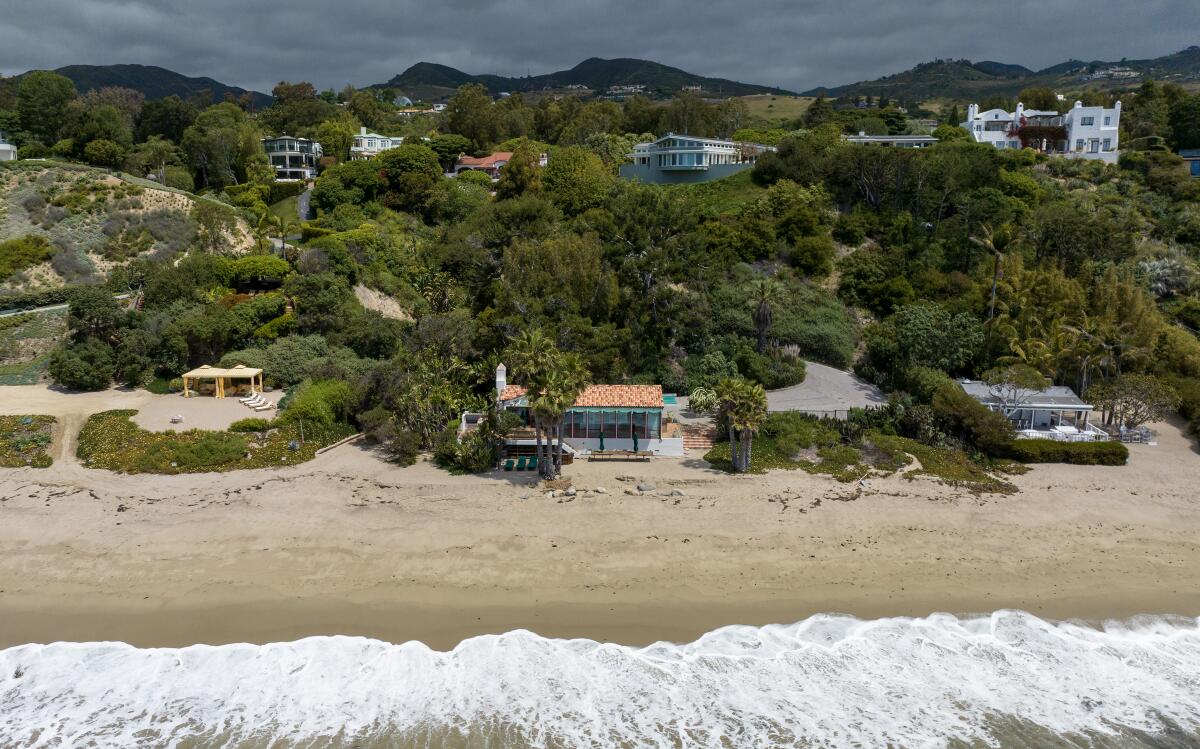 Waves lap against a beach with shoreline homes in the background.