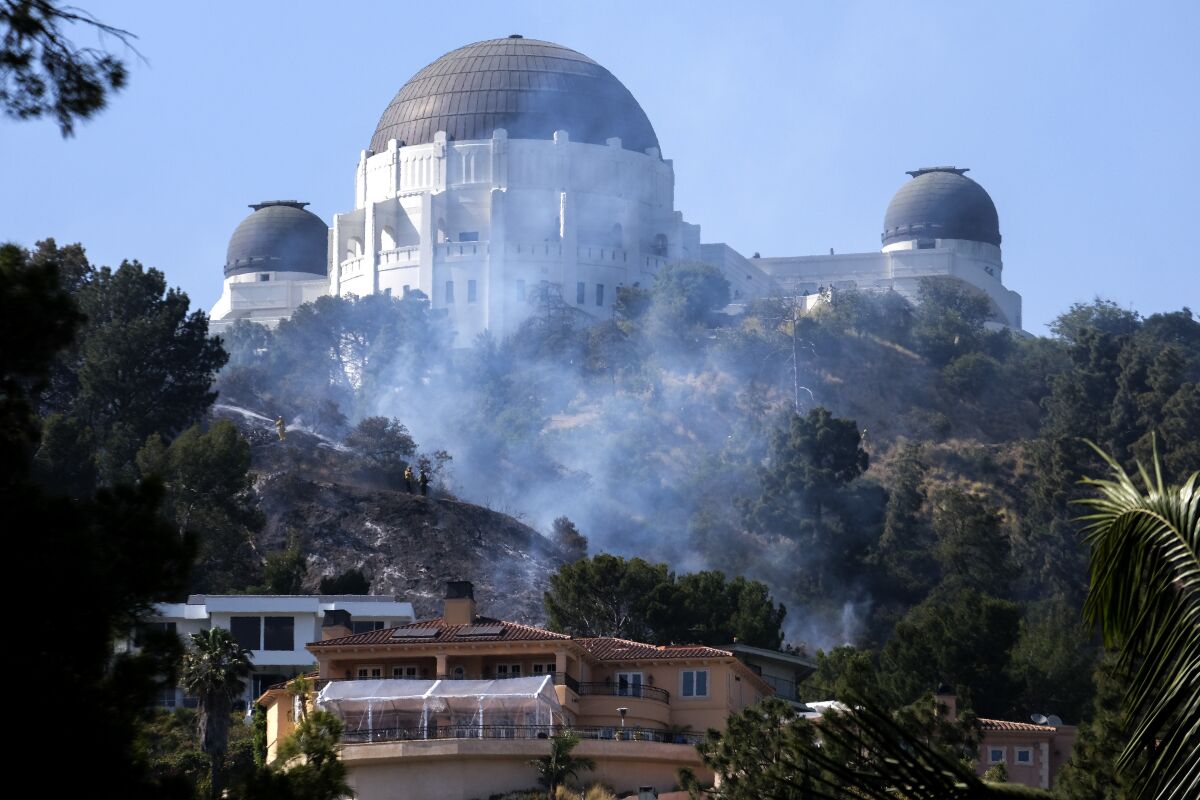 Smoke from brushfire rises between homes and the Griffith Observatory in the hills of Los Feliz in Los Angeles on Tuesday, May 17, 2022. (AP Photo/Ringo H.W. Chiu)