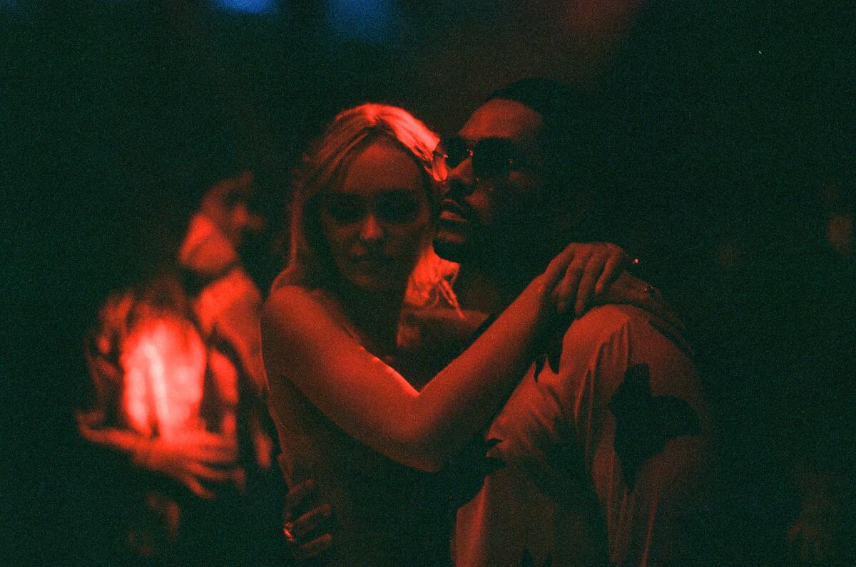 Lily-Rose Depp embraces Abel "The Weeknd" Tesfaye under dim, red lighting.